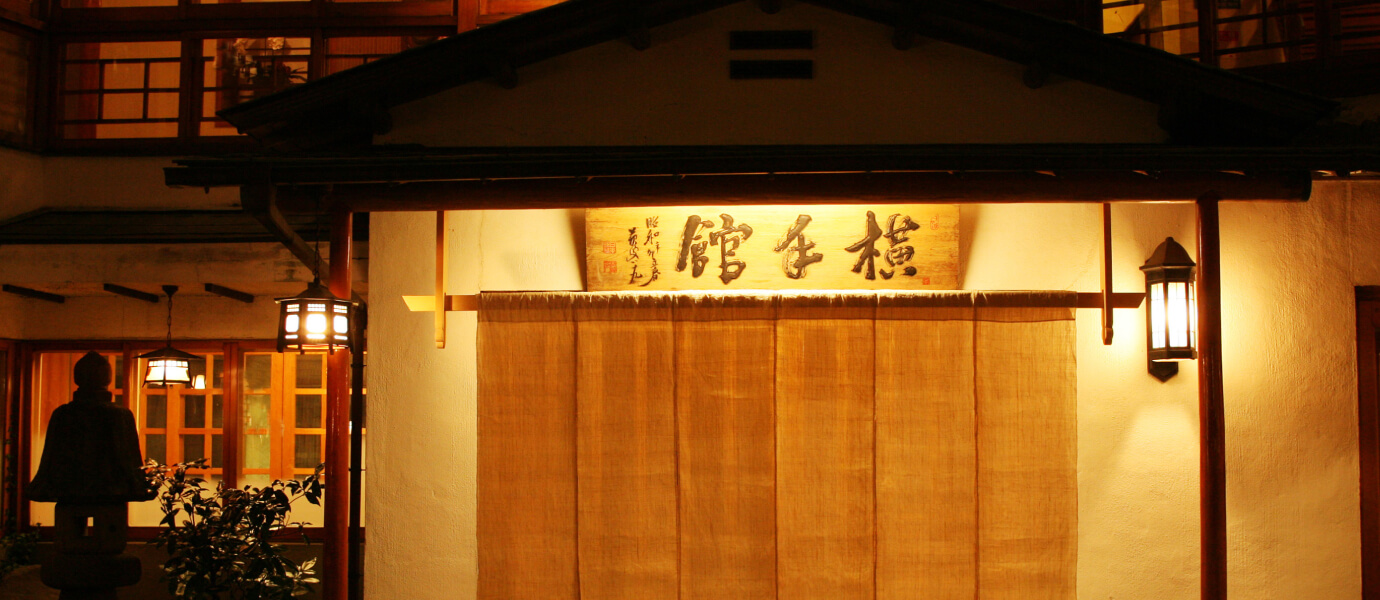 横手館 — 伊香保石段街中段 · 大正九年築の木造看板と暖簾の夜景