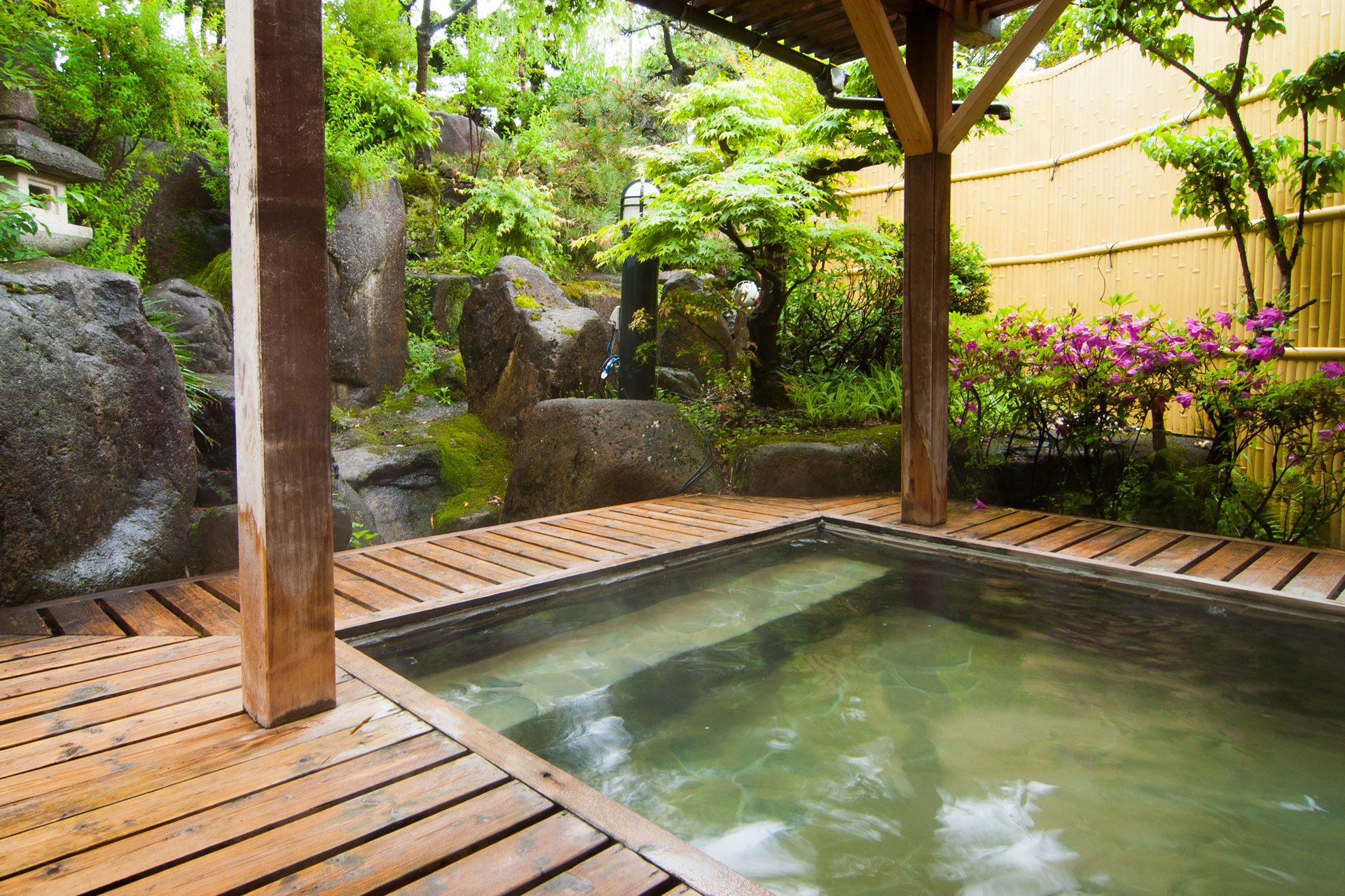 八ツ三館 露天風呂 — 飛騨古川 · 石組みと苔の中庭に面した檜の湯船、梅雨明けの緑