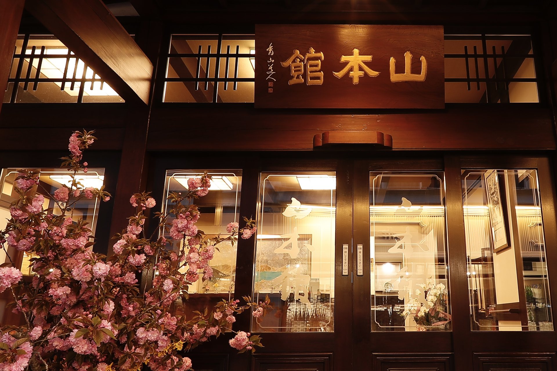草津温泉 山本館 — 玄関と桜 / 湯畑湯路の真向かい、看板を掲げた数寄屋造りの近代和風建築
