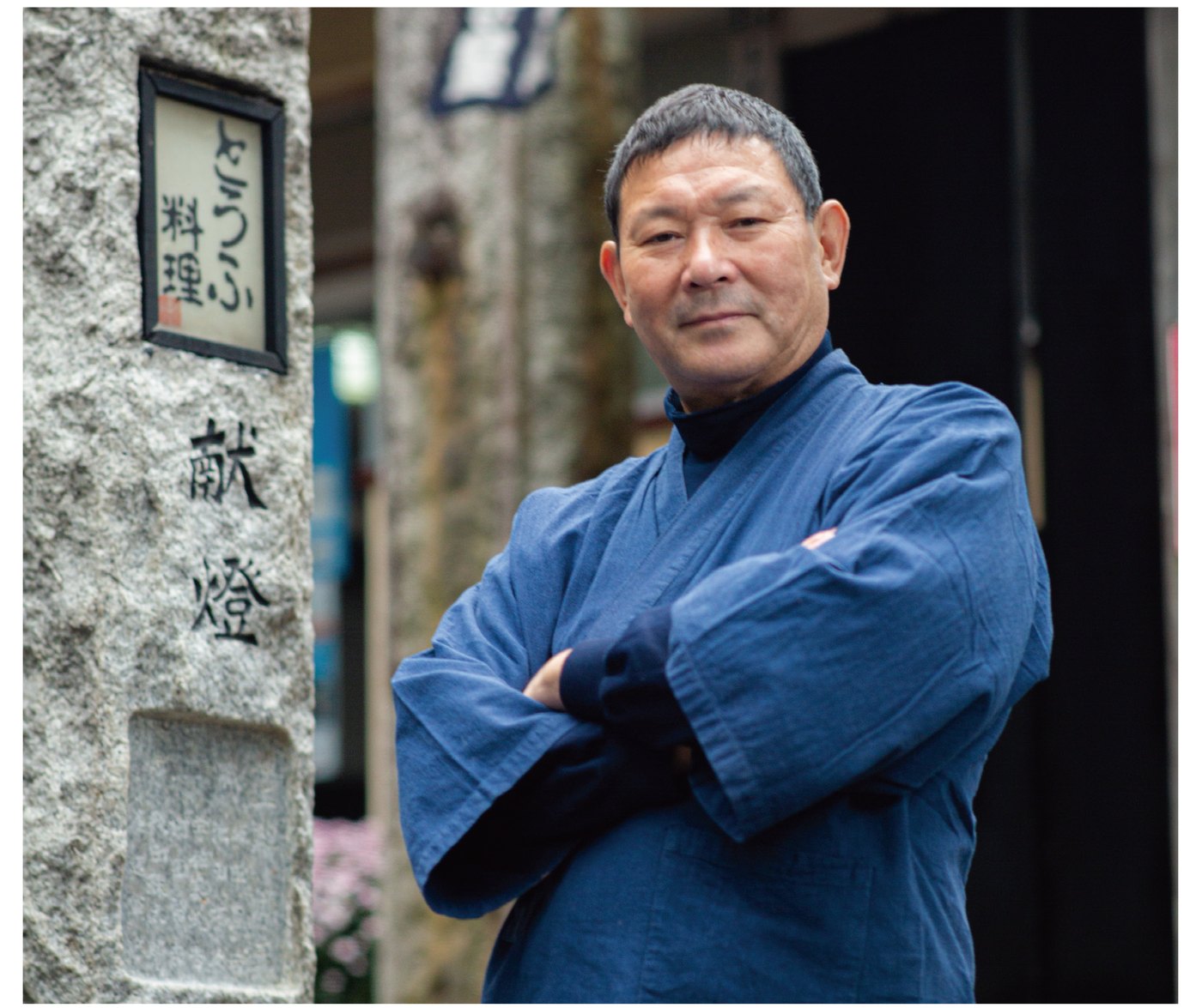 先導師旅館 古宮 第十七代当主 古宮宏和 — 「とうふ料理」の扁額を掲げた献燈の石柱を背に立つ
