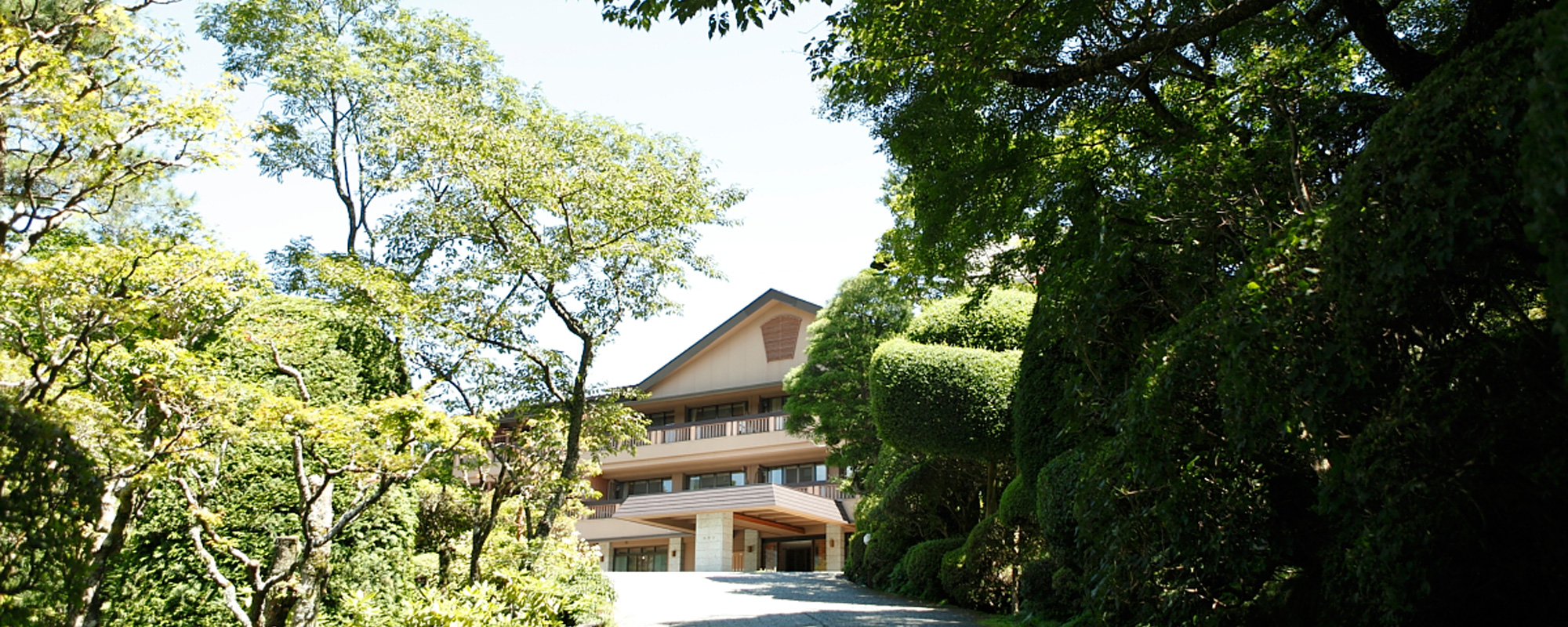 仙郷楼 本館 — 箱根仙石原 · 一万五千坪の樹林に伏せる切妻屋根の母屋と、玄関へ続く庭のアプローチ