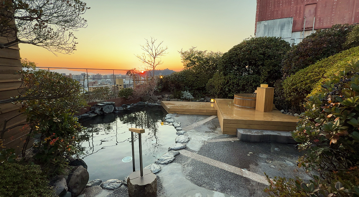 茶玻瑠 — 松山市道後湯月町 · 屋上露天風呂「星の湯」と日没時の松山市街の眺め
