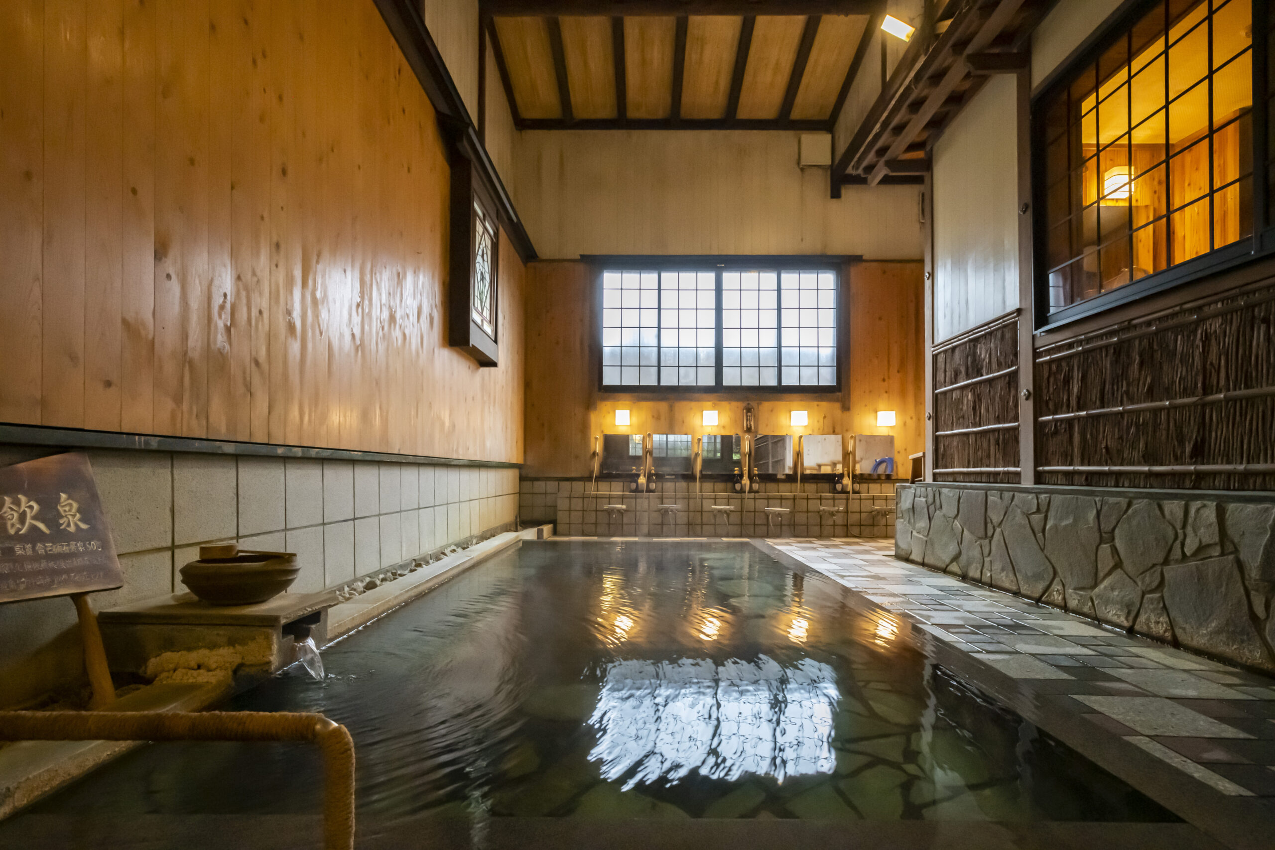 岩井屋 — 鳥取県岩美町岩井温泉 · 名物「源泉長寿の湯」、高い天井と木壁に囲まれた足元湧出の深い浴槽