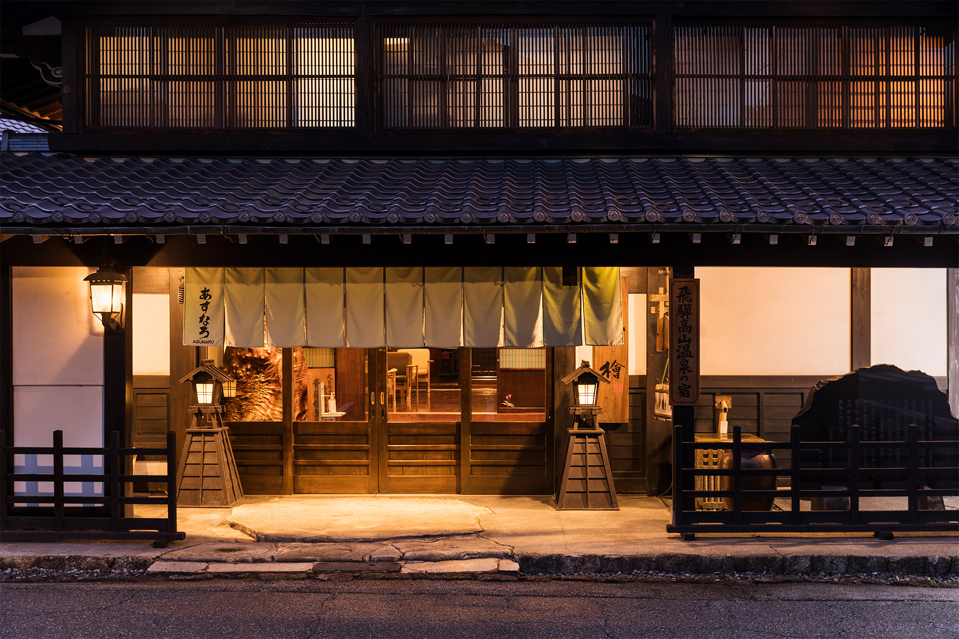 旅館あすなろ — 高山市初田町 · 暮れ方に灯が入る出格子と暖簾、瓦庇の飛騨造りの正面