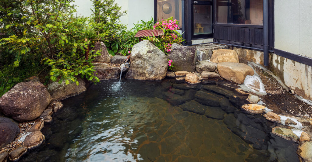 岡田旅館 和楽亭 — 奥飛騨・平湯温泉 · 岩組みの露天風呂に湯口から注ぐ源泉