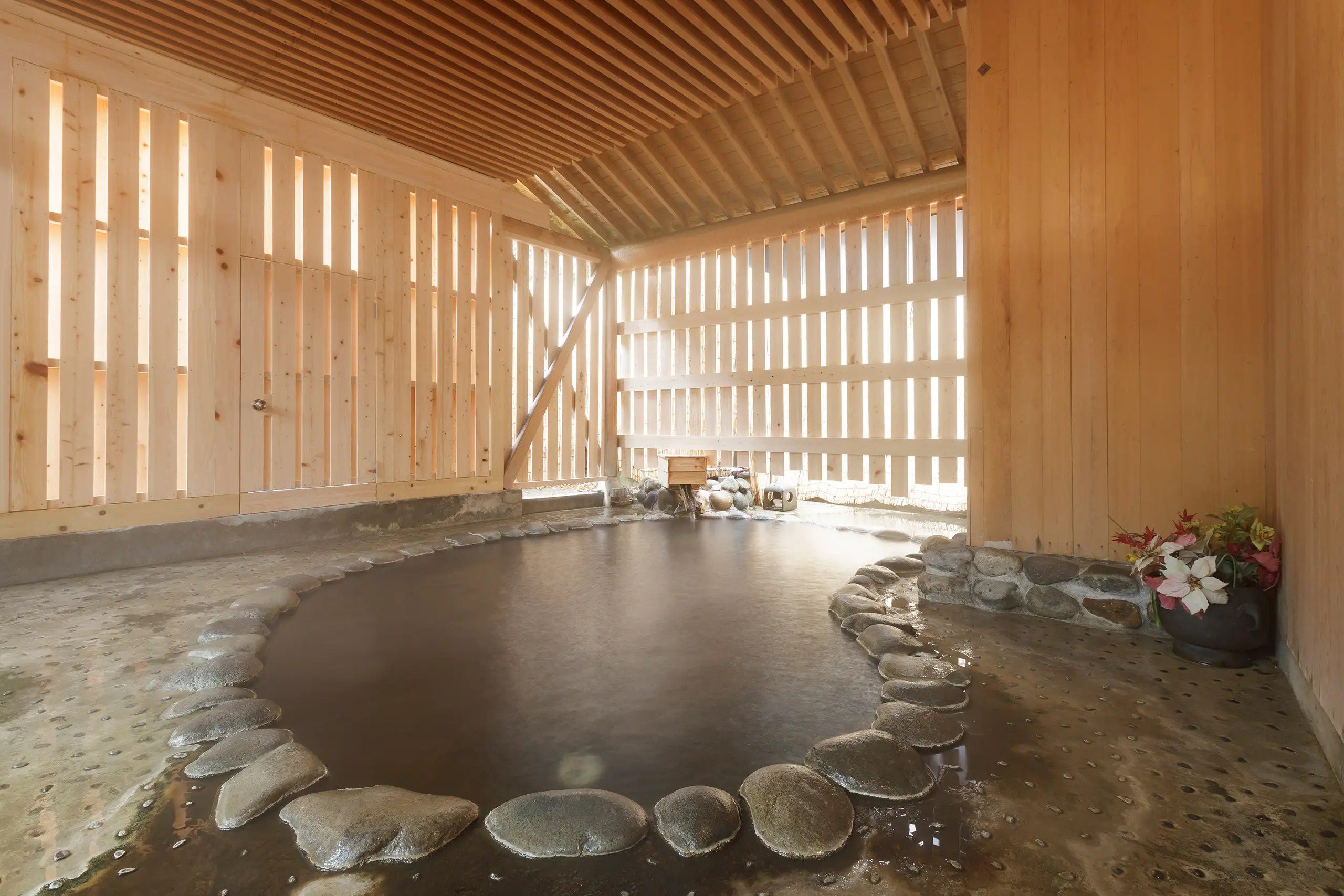 松田屋旅館 — 岩手県花巻市台温泉 · 木の格子に囲われた浴場と、石を敷いた湯船の縁