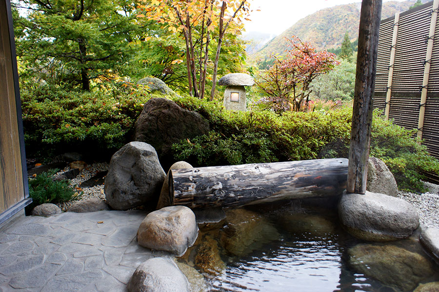 隠庵ひだ路 — 岩造りの露天風呂 · 丸太の湯口と石灯籠、山肌の紅葉を望む湯船