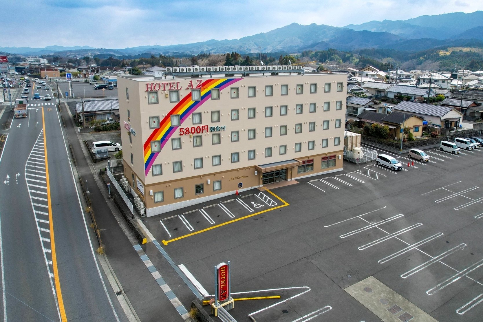 HOTEL AZ 大分三重店 — 豊後大野市三重町赤嶺 · 山並みを背にした客室棟と平面駐車場