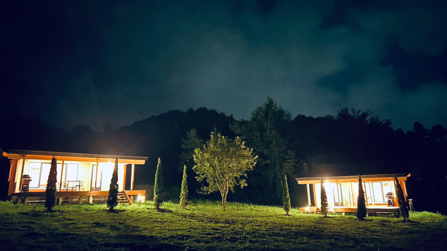 enukoti — 長野県原村・八ヶ岳西麓 · 夜の草地に灯る二棟のフィンランドログコテージ