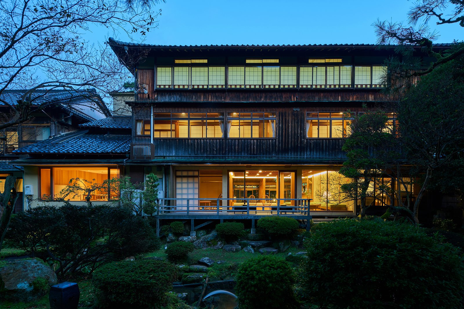 三木屋 — 城崎温泉 · 日本庭園から見上げる木造三階建ての客室棟、夕暮れの灯り