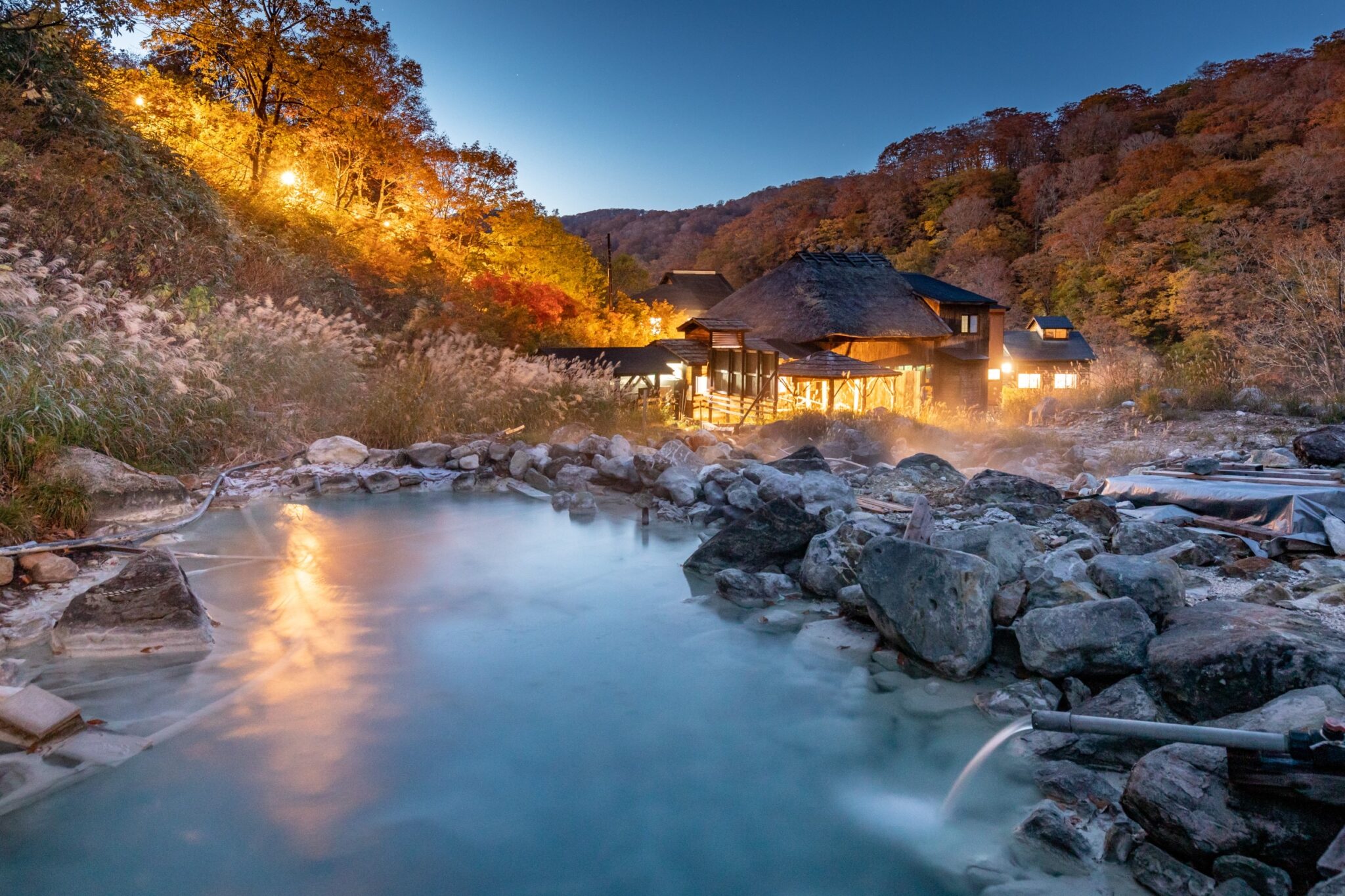 黒湯温泉 — 秋田県仙北市・乳頭温泉郷 · 夕暮れの源泉地帯と灯りのともる茅葺きの宿舎