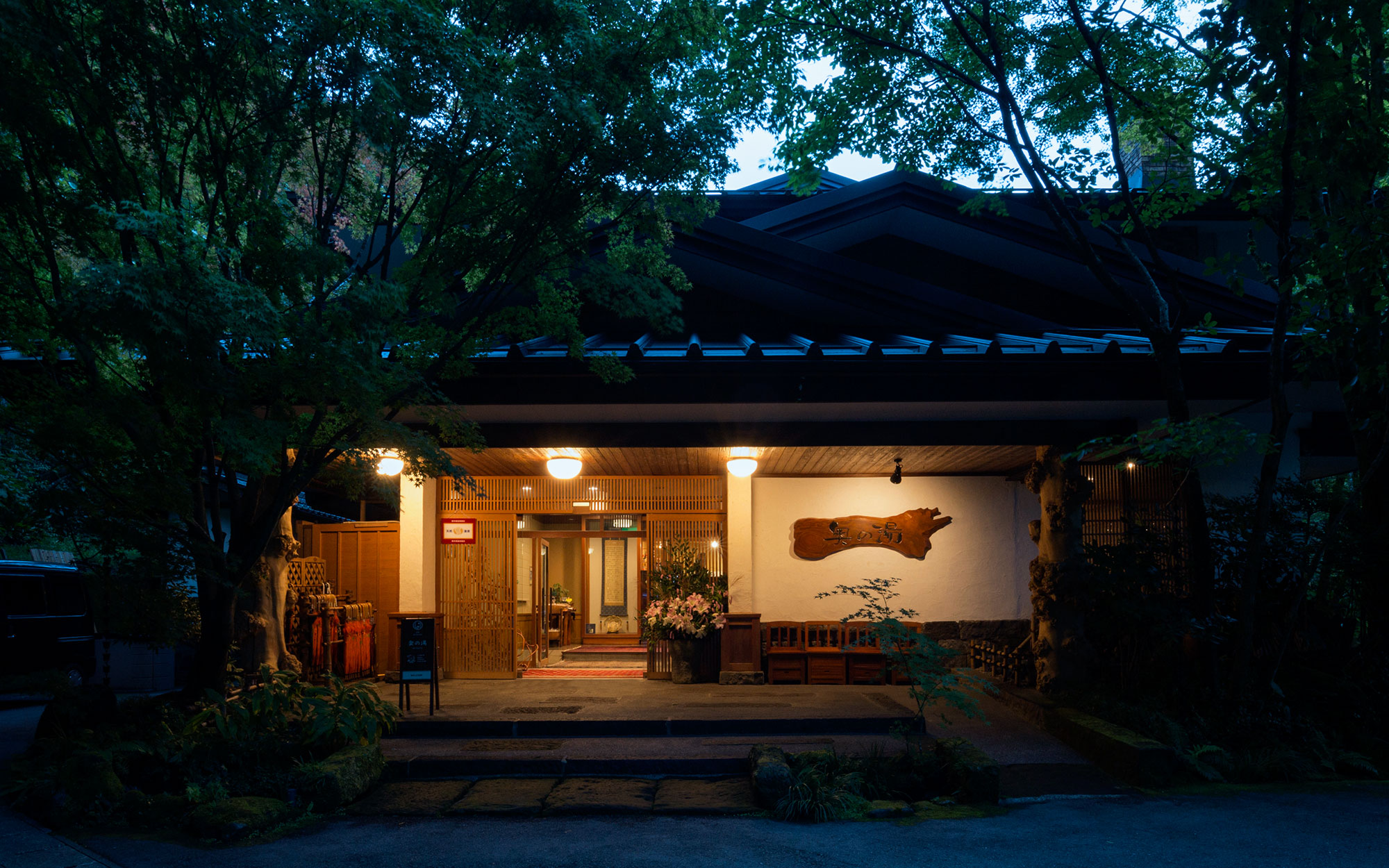 旅館 奥の湯 — 熊本県南小国町・黒川温泉 · 木立に囲まれた夕暮れの玄関と軒先の明かり
