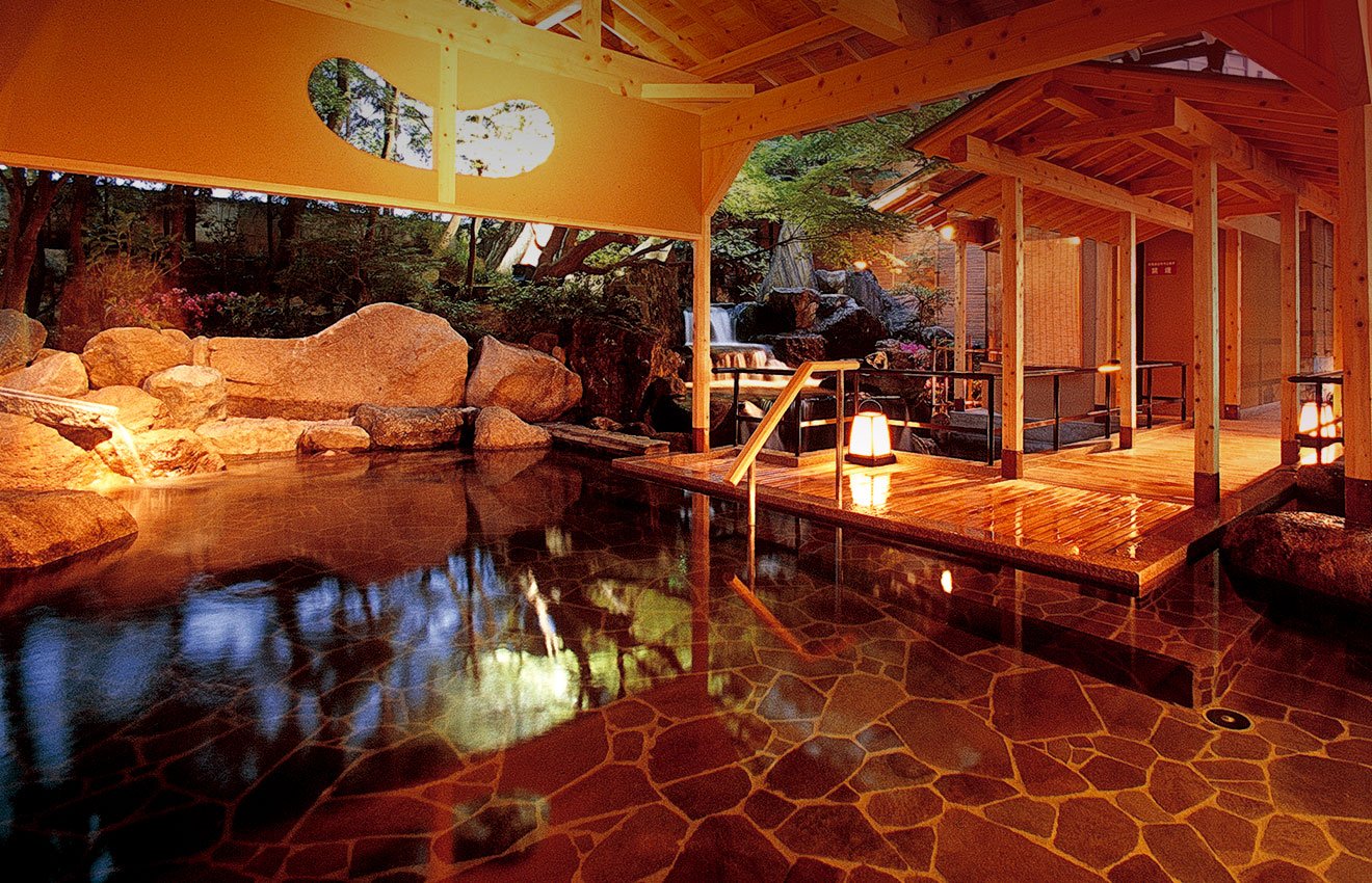 瑠璃光 — 加賀市山代温泉 · 庭園に面した岩造りの露天風呂と湯屋の夜景