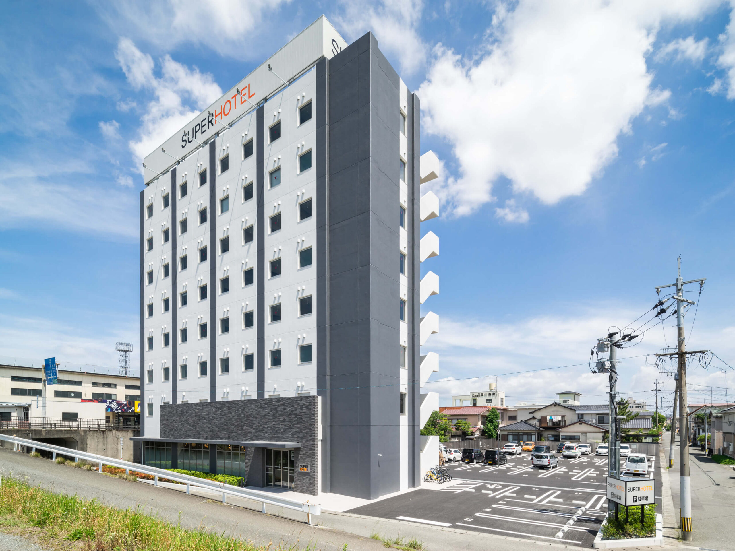 スーパーホテル熊本・八代 — 熊本県八代市夕葉町 · 隣接の平面駐車場をもつ白い外観の宿