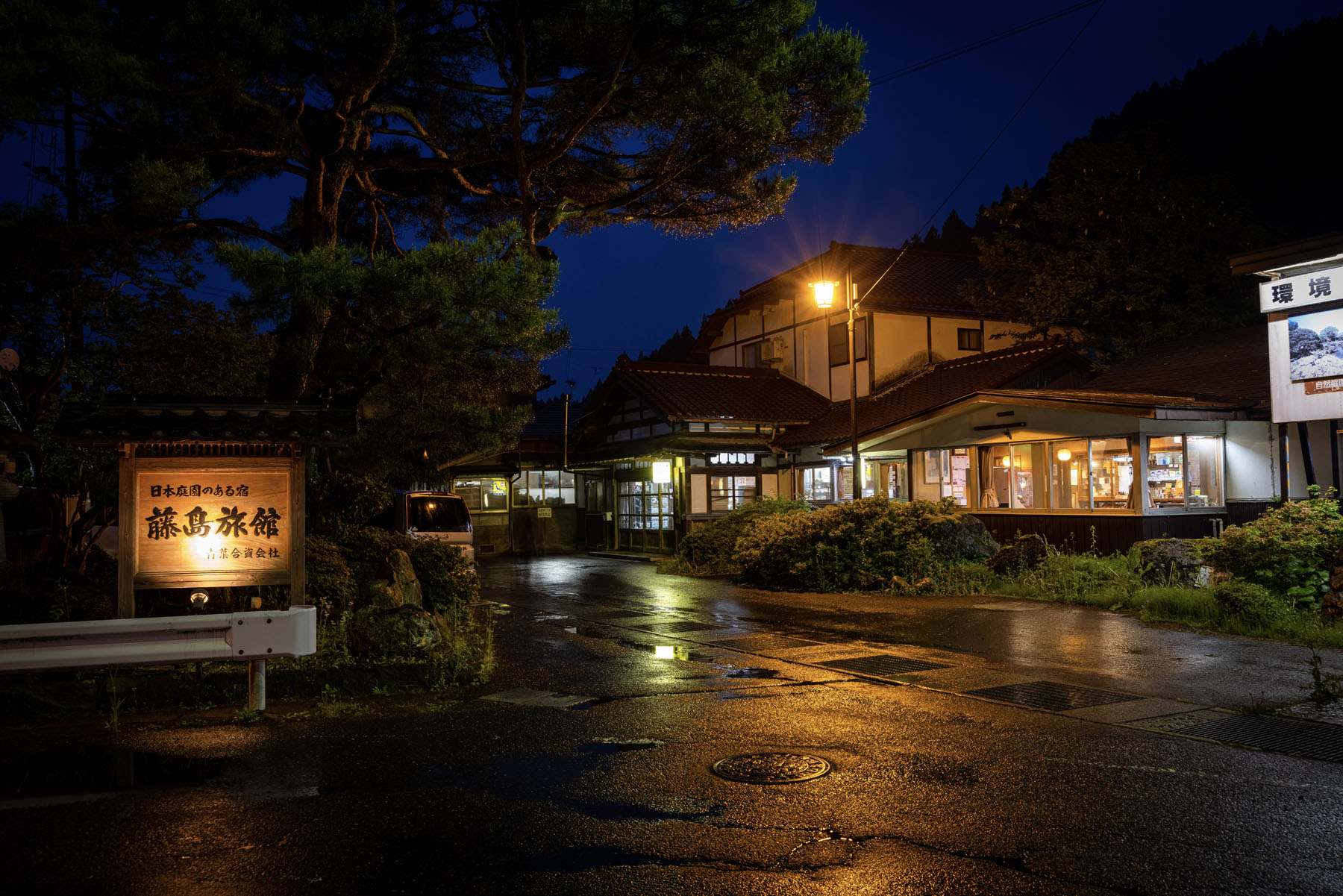 藤島旅館 — 大崎市川渡温泉 · 雨上がりの夜に灯がともる木造の湯治宿の外観